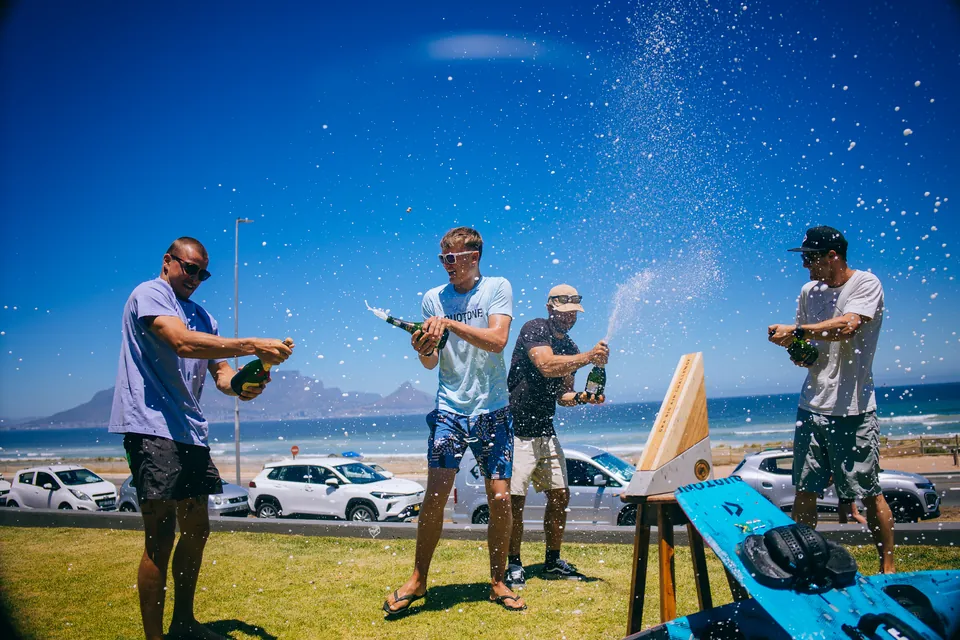 A group of riders celebrating together, spraying champagne at a beachside event